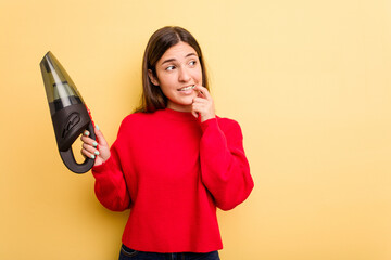 Young caucasian woman holding a hand vacuum cleaner isolated on yellow background relaxed thinking about something looking at a copy space.