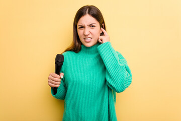 Young caucasian singer woman isolated on yellow background covering ears with hands.