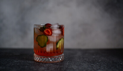 Fresh strawberry cocktail with berries, with pieces of cucumber and with ice on a gray background.