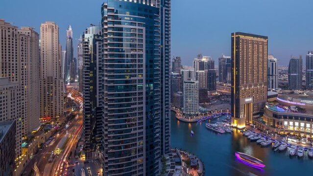 Evening illumination of Dubai Marina day to night transition aerial timelapse, UAE. Modern skyscrapers and residential buildings. Yachts and boats near shoping mall on artificial canal city