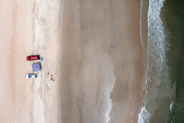 Aerial View top down of four wheel drive vehicles on the beach near the ocean with a tent on the sand