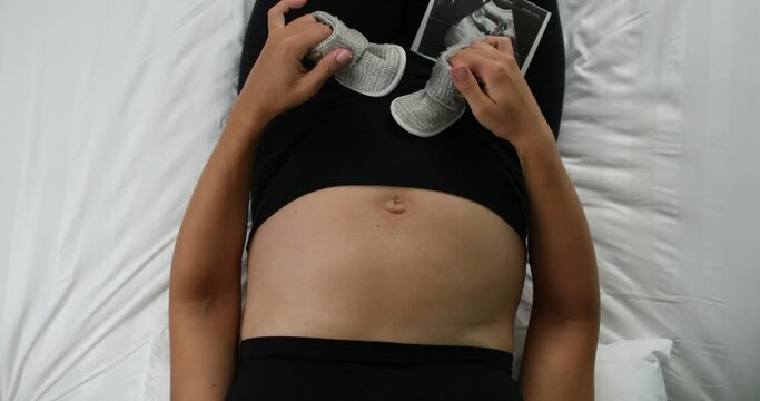 Pregnant mother holding baby clothes in hands.