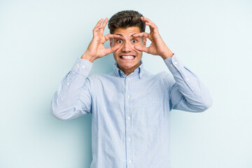 Young caucasian man isolated on blue background keeping eyes opened to find a success opportunity.