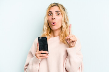 Fototapeta premium Young caucasian woman holding mobile phone isolated on blue background having some great idea, concept of creativity.