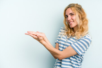 Young caucasian woman isolated on blue background holding a copy space on a palm.