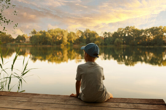 Boy on a pier by the lake. the child looks at the lake, sunset, nature. Child is sitting on the pier. Photography. Landscapes