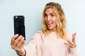 Young caucasian woman holding mobile phone isolated on blue background