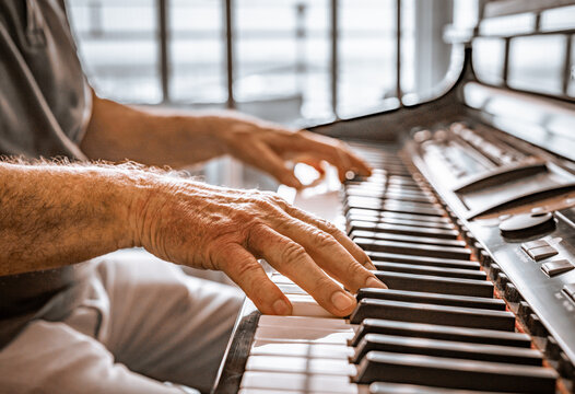 Old person's hands playing the piano. Close up view of skin texture and piano keys.