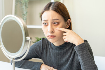 Bored, insomnia asian young woman, girl looking at mirror hand touching under eyes with problem of...