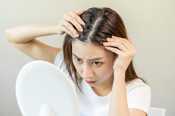 Damaged Hair, face serious asian young woman worry looking at scalp in mirror, hand in break into...