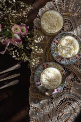 Pavê de abacaxi e coco montado em copos. Porções individuais. Lanche da tarde. Mesa bonita com crochê e flores. Vista de cima.