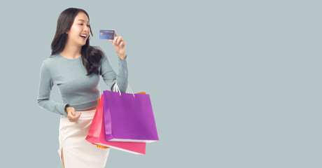 Young asian lady using credit card holding shopping bags isolated over pastel green background and...