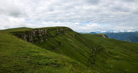Panoramic view of green mountains and hills from the Bermamyt plateau in Karachay-Cherkessia in Russia on a cloudy summer day and a space for copying