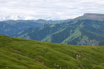 Panoramic view of green mountains and hills from the Bermamyt plateau in Karachay-Cherkessia in Russia on a cloudy summer day and a space for copying