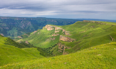 Fototapeta na wymiar Panoramic view of green mountains and hills from the Bermamyt plateau in Karachay-Cherkessia in Russia on a cloudy summer day and a space for copying