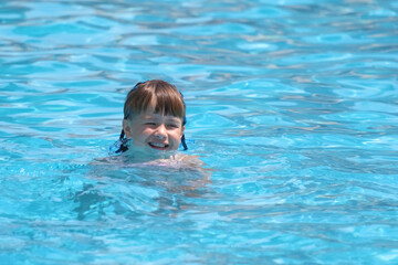 Fototapeta na wymiar Child girl learns to swim. Funny face with closed eyes on bright blue rippled water surface