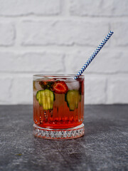 Fresh strawberry cocktail with straw, berries, with pieces of cucumber and with ice on a gray and bricks background.
