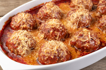 Meat balls on a white plate with tomato sauce and melted cheese