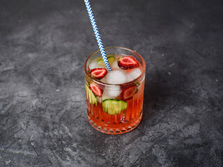 Fresh strawberry cocktail with straw, berries, with pieces of cucumber and with ice on a dark background. Space for text.