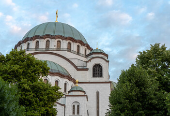 Fototapeta na wymiar Cloudy sky with green tree and Saint Sava and christian catedral in the capital Belgrade of Serbia