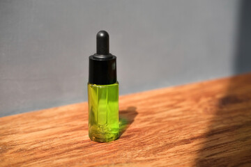 cosmetic bottle with green serum for skin with dropper stands on wooden surface on background of gray wall