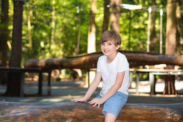 a happy boy sits on a log in the park, a schoolboy spends summer in a camp in nature