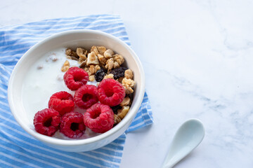 Granola with raspberries and greek yogurt in a bowl on white marble table background. Top view, flat lay, copy space. Healthy breakfast concept.