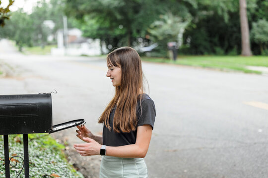 A teen brunette girl with long hair checking the mailbox for letters and packages.
