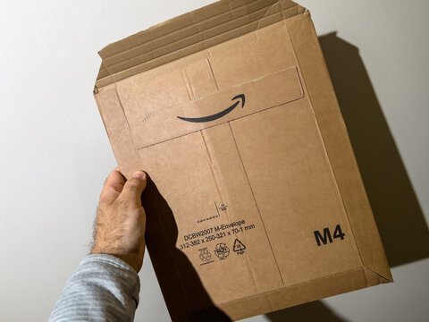 Paris, France - Apr 24, 2022: Pov male hand holding new Amazon Prime cardboard parcel with the iconic smiling arrow logotype