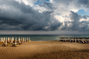 Beautiful sandy beach with closed parasols and sunbeds just after a powerful storm