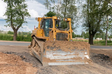 Obraz premium Crawler bulldozer clears the ground with a metal shield. Landscaping. Road construction works.