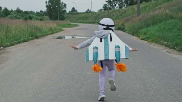 Little girl wearing white helmet, jetpack and running on rural road like aviator in slow motion. Tracking of kid. 4K, UHD
