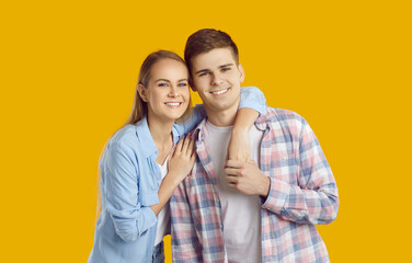 Happy young Caucasian couple man and woman smiling posing together with loved one or best friend rejoicing at meeting and looking at camera dressed in casual clothes stands in yellow studio