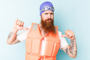 Young caucasian man wearing life jacket isolated on blue background feels proud and self confident,...