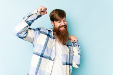 Young caucasian red-haired man isolated on blue background celebrating a special day, jumps and raise arms with energy.