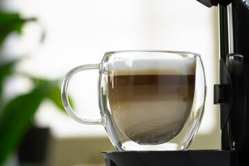 Coffee capsule machine pouring cappuccino into glass cup