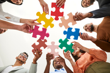 Diverse multiracial multi ethnic team of happy smiling adult men and women holding colorful jigsaw puzzle parts, bottom view, from below. Modern business, teamwork, education, innovative ideas concept