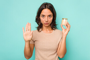 Young hispanic woman holding yogurt isolated on blue background standing with outstretched hand showing stop sign, preventing you.