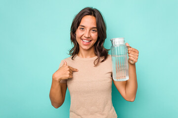 Young hispanic woman holding a water of jar isolated on blue background person pointing by hand to a shirt copy space, proud and confident
