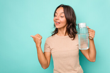 Young hispanic woman holding a water of jar isolated on blue background points with thumb finger away, laughing and carefree.