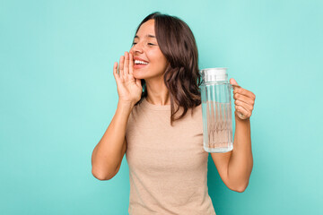 Young hispanic woman holding a water of jar isolated on blue background shouting and holding palm near opened mouth.