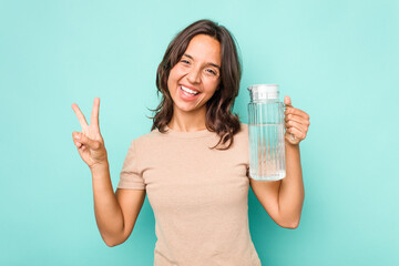 Young hispanic woman holding a water of jar isolated on blue background joyful and carefree showing a peace symbol with fingers.