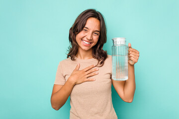 Young hispanic woman holding a water of jar isolated on blue background laughing and having fun.