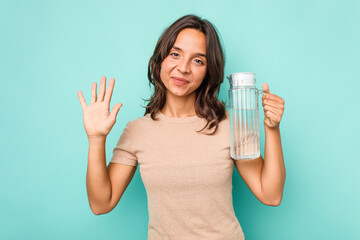 Young hispanic woman holding a water of jar isolated on blue background smiling cheerful showing number five with fingers.