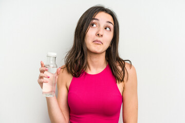 Young caucasian woman holding a bottle of water isolated on white background shrugs shoulders and open eyes confused.