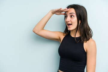 Young caucasian woman isolated on blue background looking far away keeping hand on forehead.