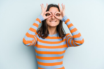 Young caucasian woman isolated on blue background showing okay sign over eyes