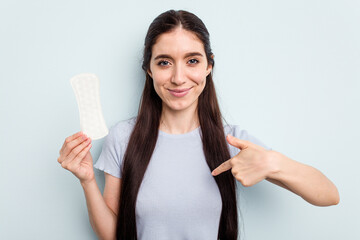 Young caucasian woman holding a sanitary napkin isolated on blue background person pointing by hand to a shirt copy space, proud and confident