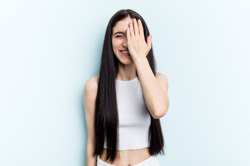 Obraz premium Young caucasian woman isolated on blue background having fun covering half of face with palm.