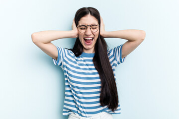 Young caucasian woman isolated on blue background covering ears with hands trying not to hear too loud sound.